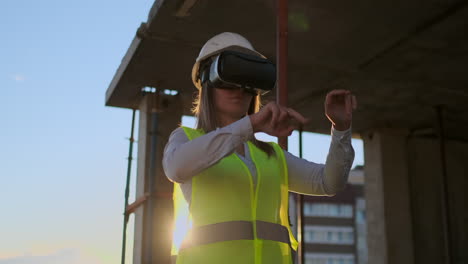 Eine-Erfahrene-Ingenieurin-Mit-VR-Brille-Und-Helm-überprüft-Den-Baufortschritt-Eines-Wolkenkratzers-Und-Bewegt-Bei-Sonnenuntergang-Ihre-Hände,-Um-Den-Bauplan-Zu-Visualisieren